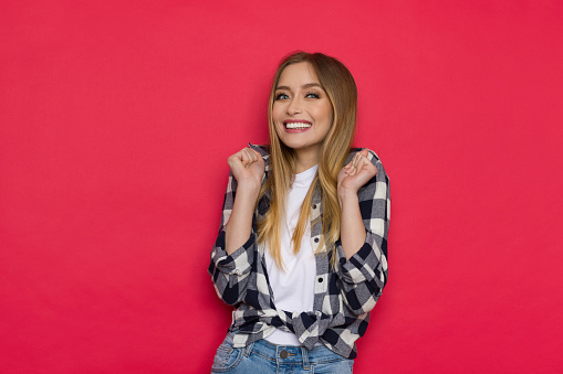 An excited young woman is gesturing and smiling. Waist up studio shot on red background.