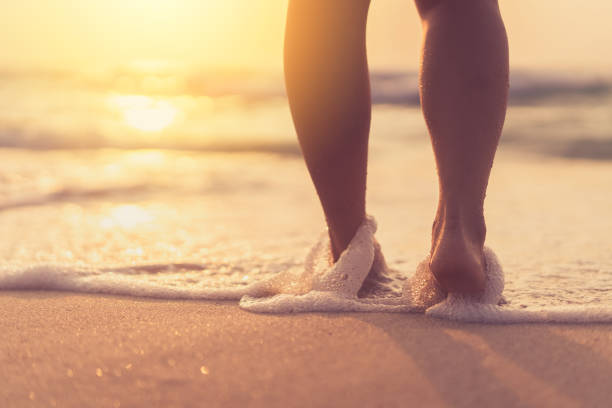 istock Close up woman legs walking on tropical sunset beach with smooth wave and bokeh sun light wave abstract background. 1307201955