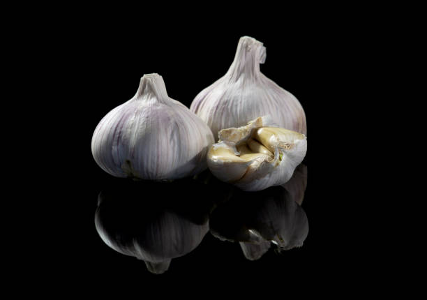 istock Two whole garlic heads and a half, with a reflection, on a black isolated background. Close-up, copy space 1307203742