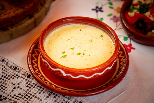 Creamy lamb soup with parsley on top, served in pottery bowl on restaurant table, traditional Serbian starter