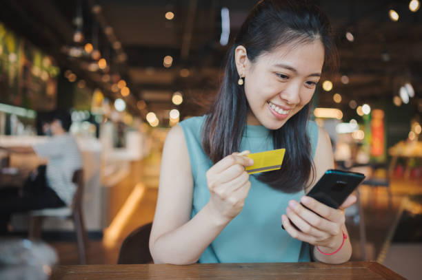 cheerful young asian woman shopping online with smartphone and making mobile payment with credit card on hand, receiving a parcel by home delivery service. technology makes life so much easier - shopping e commerce internet credit card imagens e fotografias de stock