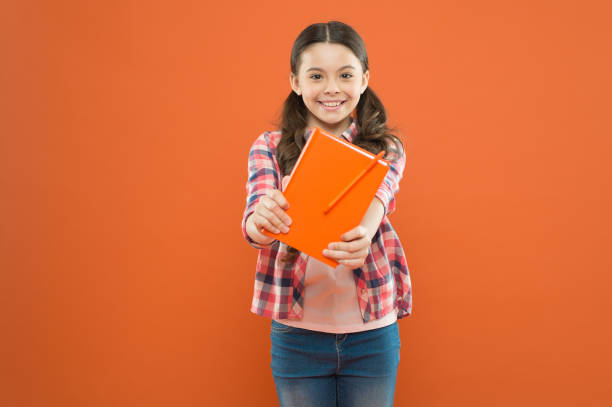 istock share knowledge. poetry and novel. modern education. writing notes. kid diary. literature lesson. back to school. school girl read book on orange background. happy little girl with notebook 1307208393