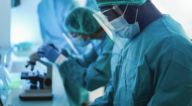 istock Medical workers in hazmat suit working with computer and micoroscope inside hospital lab during coronavirus outbreak - Focus on african nose 1307210863