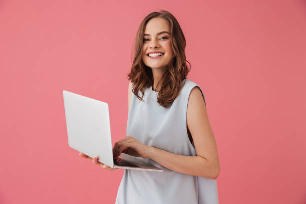 Cheerful young woman using laptop computer. Looking camera. Image of cheerful young woman standing isolated over pink background using laptop computer. Looking camera. isolated color stock pictures, royalty-free photos & images