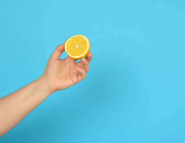 istock female hand holds half a yellow lemon on a blue background 1307212617