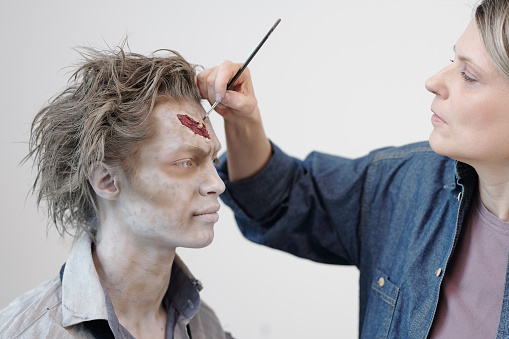 Artista de rostro contemporáneo con pincel aplicando maquillaje zombi en la cara del joven empresario o actor photo