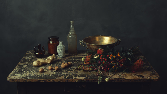 Old worn wooden table with two glass bottles, a glass pitcher, a glass jar, a bronze bowl, ginger and walnuts and flowers.