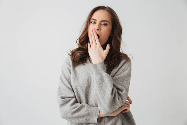 Tired brunette woman in sweater yawns and covering her mouth stock photo