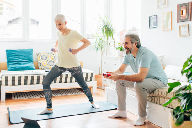 istock Senior woman doing exercises while senior man playing video games on couch 1307220020
