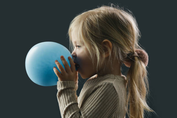 una niña haciendo estallar un globo. pulmóns de entrenamiento infantil haciendo ejercicio de respiración, estudio rodado sobre fondo negro. - balloon blowing inflating child fotografías e imágenes de stock