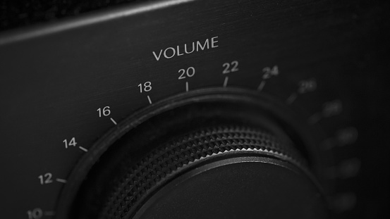 Low key black and white macro close-up of the volume knob on an old stereo, both knob and device are black, text and numbers are white