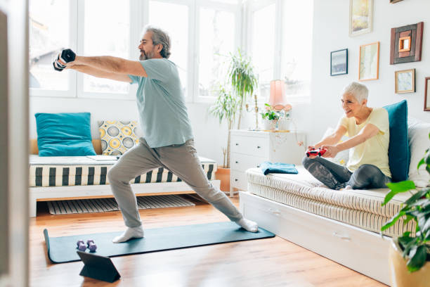 istock Senior man doing exercises while senior woman playing video games on couch 1307222930