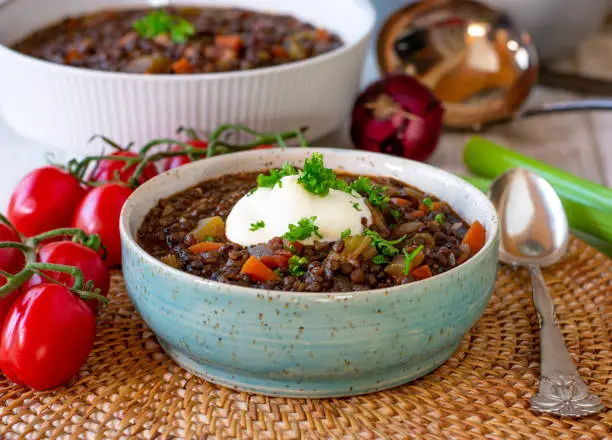 fresh and homemade cooked lentil stew with beluga lentils and vegetables served in a bowl with spoon. Ready to eat