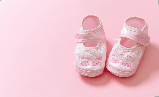 Baby shower, girl christening concept. Baby pink shoes on pink color background. Itâs a girl newborn announcement template. Infant soft female footwear, closeup view