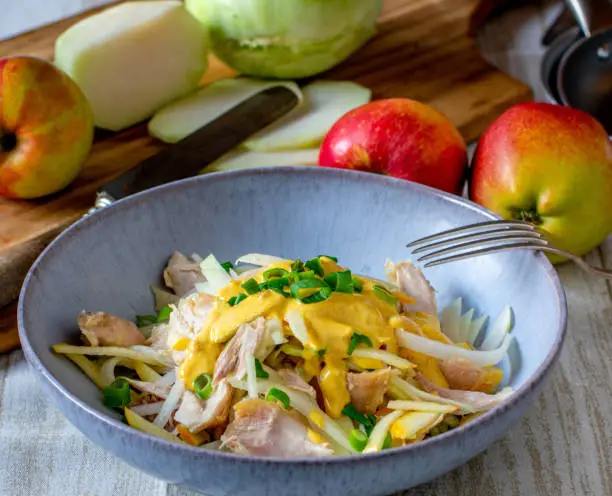 Raw Apple Kohlrabi salad with chicken meat and curry dressing served in a bowl on kitchen table. Ready to eat