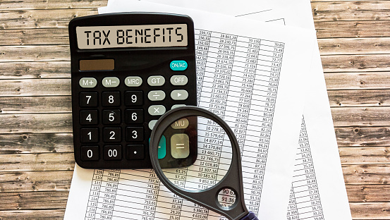 the inscription TAX BENEFITS on the display of the calculator, the documents are on a wooden table