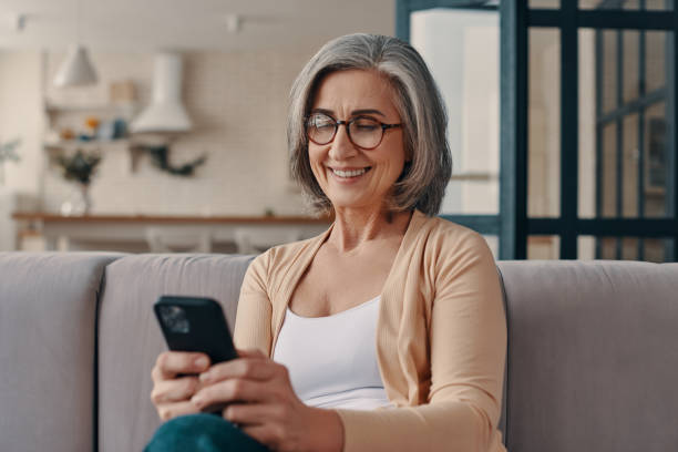 Beautiful senior woman in casual clothing Beautiful senior woman in casual clothing using her smart phone while sitting on the sofa at home older women stock pictures, royalty-free photos & images