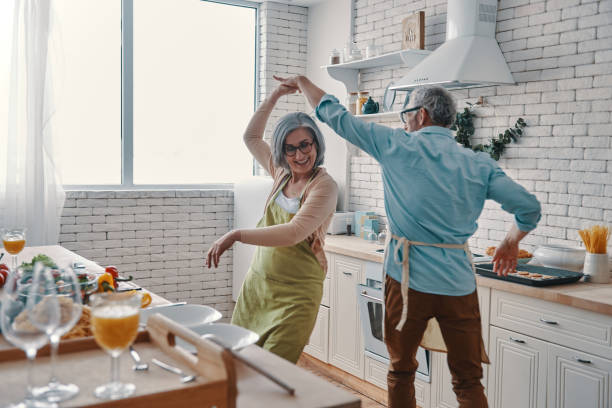 Beautiful playful senior couple Beautiful playful senior couple in aprons dancing and smiling while preparing healthy dinner at home lifestyle couple stock pictures, royalty-free photos & images