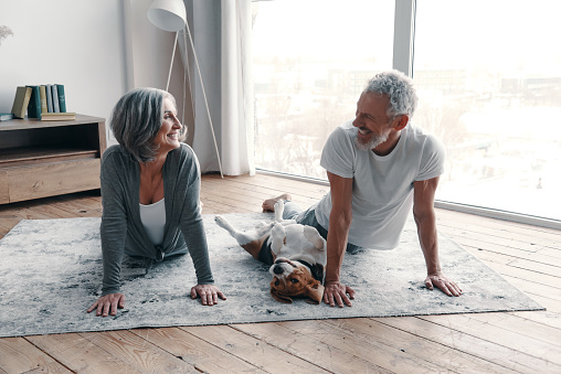 Loving senior couple in sports clothing doing yoga and smiling while spending time at home with their dog