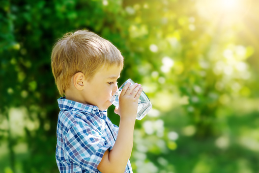 Cute boy drinking a glass of pure water in nature. Concept of the provision of clean, mineral aqua in the world.