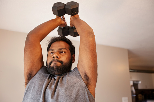 Early 30s Indian man exercises at home with dumbbells