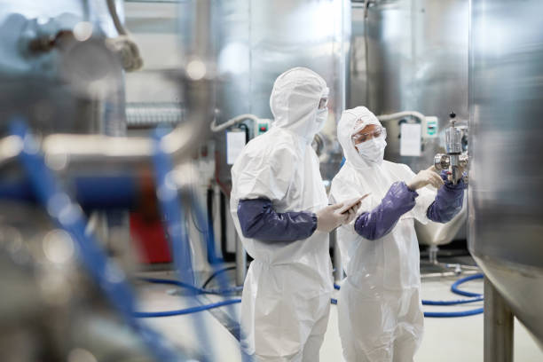 Two Workers Controlling Pharmaceutical Production Side view portrait of two workers wearing protective suits while using equipment at modern chemical plant, copy space chemical stock pictures, royalty-free photos & images