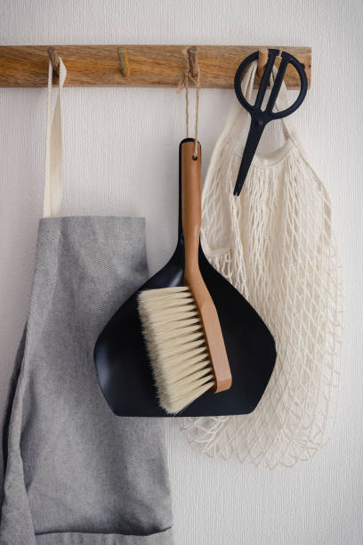 istock Hook hanger with black scissors, grey apron, white eco bag, broom and scoop hanging on a white wall in the modern kitchen 1307246013
