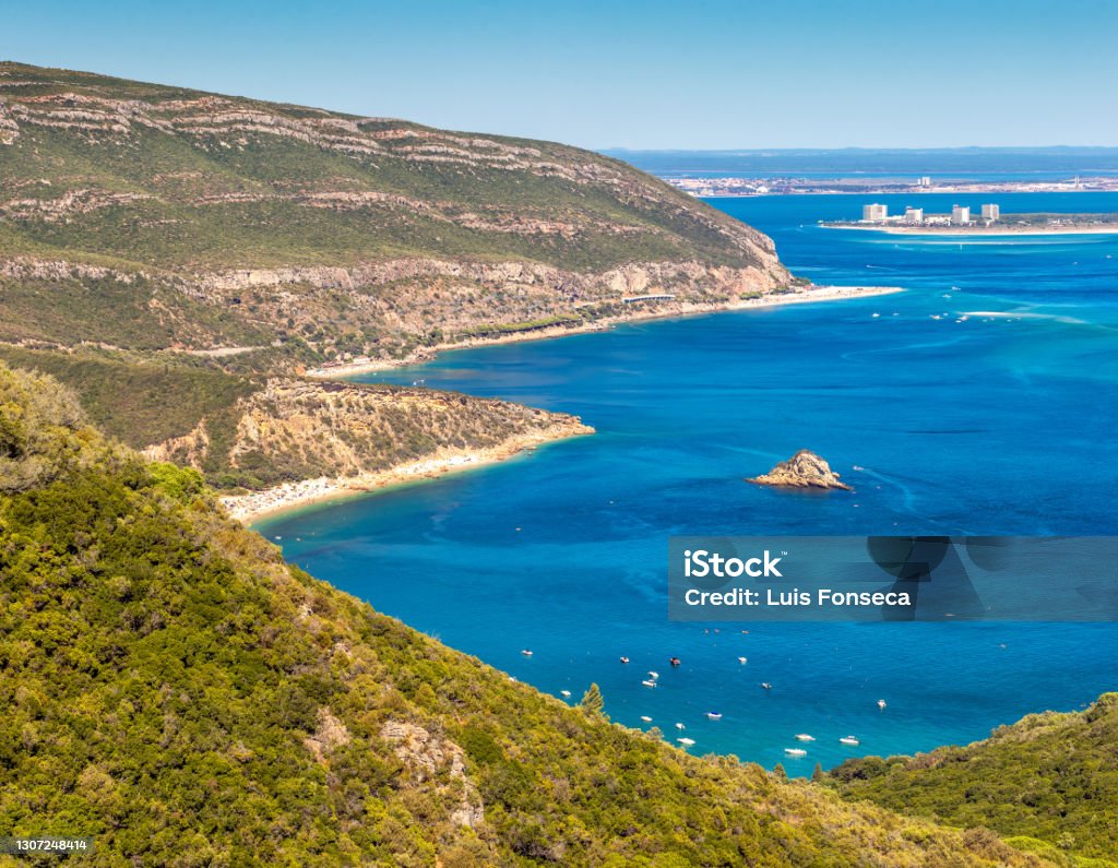 View of the southern slope of the Serra da Arrábida in Portugal, with the bay of Portinho da Arrábida, the beaches of Galápos and Figueirinha and Tróia in the background. The Arrábida Natural Park is a biogenetic reserve composed of marine and terrestrial areas.
It rests on a limestone massif that falls over the sea on large cliffs, looking like a wall cut out by coves, beaches of fine sand and transparent waters. Beach Stock Photo