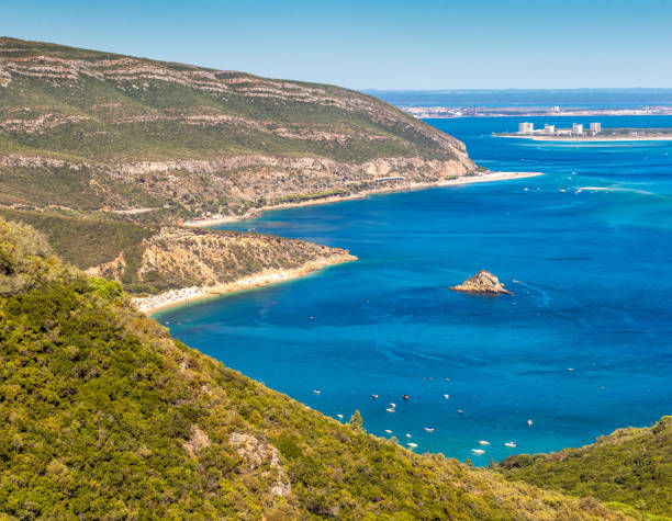 View of the southern slope of the Serra da Arrábida in Portugal, with the bay of Portinho da Arrábida, the beaches of Galápos and Figueirinha and Tróia in the background. The Arrábida Natural Park is a biogenetic reserve composed of marine and terrestrial areas.
It rests on a limestone massif that falls over the sea on large cliffs, looking like a wall cut out by coves, beaches of fine sand and transparent waters. setúbal city portugal stock pictures, royalty-free photos & images