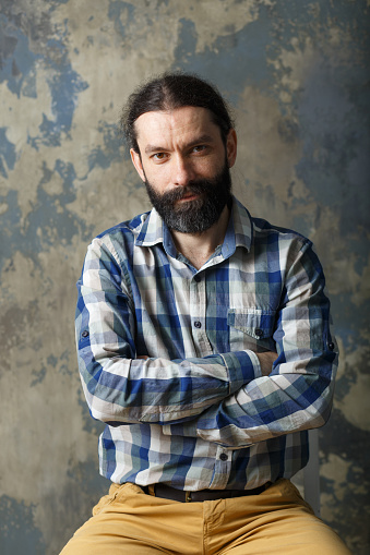 Portrait of a pleasant young man with a beard and mustache in a plaid shirt on an abstract background