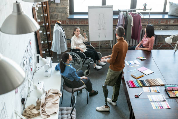 istock Young disable female designer by whiteboard and other colleagues listening to confident man 1307252882