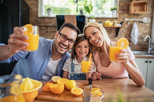 Family.Happy mother and daughter drink orange juice in the kitchen and have fun together.