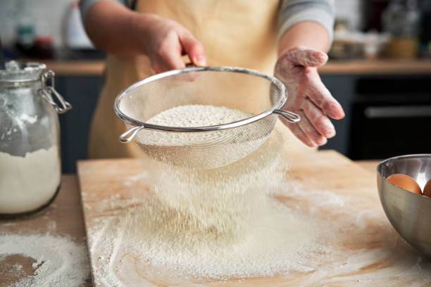 close up of sifting flour in domestic kitchen - sifting imagens e fotografias de stock