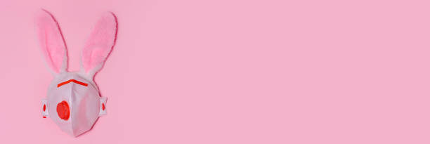 istock Pink bunny rabbit with face protective mask on pink background. Easter quarantine concept.Copy space for text, top view, flat lay. Banner 1307254598