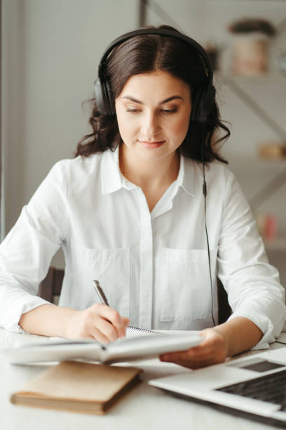 istock Woman in headphones work on laptop making notes 1307256893