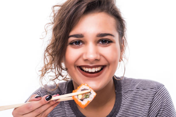 istock Young woman happily eating sushi rolls isolated on white background 1307257104