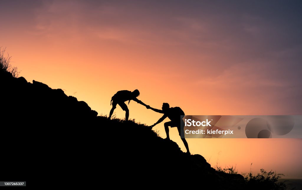 Young people on mountain hike Hikers helping each other. Assistance Stock Photo