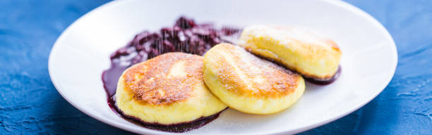 frühstück und leckeres konzept - pfannkuchen aus hüttenkäse mit marmelade, blauem hintergrund. mit puderzucker bestreuen. - cheesecake syrup cottage cheese cream stock-fotos und bilder