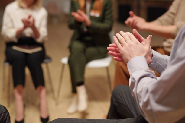 istock Patients of mental support group clapping hands while sitting in circle during psychological session 1307266701