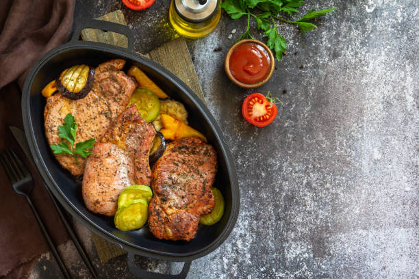 déjeuner ou dîner de régime cétogène d’été. longe de porc grillée sur l’os avec des légumes cuits au four dans une poêle en fonte sur un comptoir en pierre foncée. vue supérieure à plat. espace de copie. - barbecue lunch dinner loin photos et images de collection