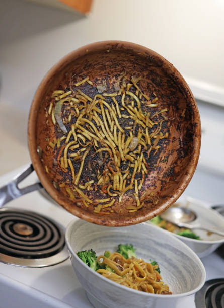 Asian noodles and sliced onions remain stuck to the bottom of a non-stick frying pan. Domestic kitchen in Canada.