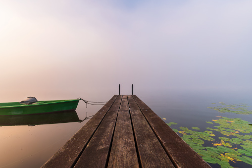 A jetty with boat shrouded in fog in warm morning light in Bavaria. Soothing landscape photo of Hopfensee lake in Allgäu. Well suited for quotes or as background.
