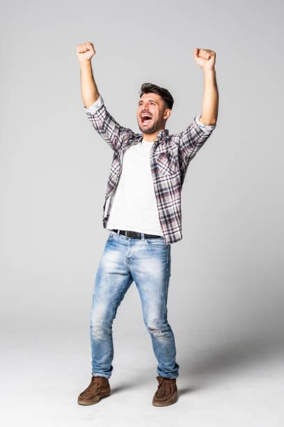 istock Casual handsome young man shouting for joy raising his hands above his head isolated on white background 1307278479