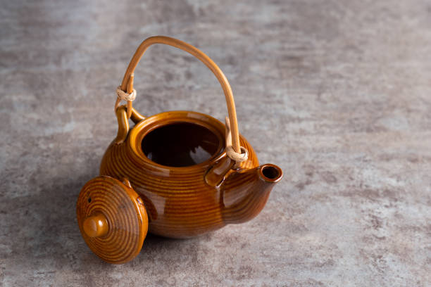 A brown teapot with a bamboo handle and an open lid on a stone countertop. copyspice.