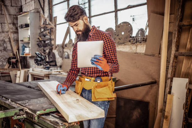 istock Young man at carpentry cutting wood with a circular saw and using digital tablet. 1307279805