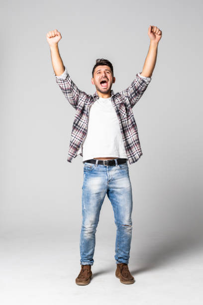 istock Casual handsome young man shouting for joy raising his hands above his head isolated on white background 1307280908