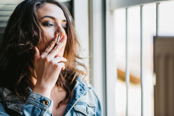 istock Woman smoking a cigarette by window 1307281379