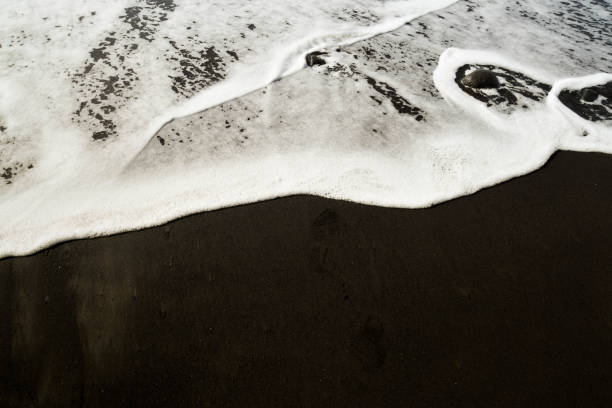 istock Contrast between white sea foam and black volcanic sand 1307282390