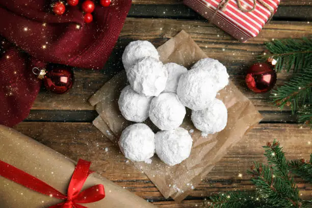 Tasty snowball cookies and Christmas decorations on wooden table, flat lay
