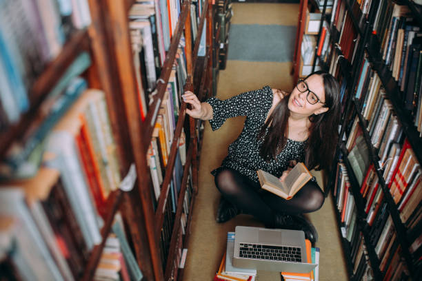 istock Sweet young student girl sitting on library floor and reading a book 1307291503
